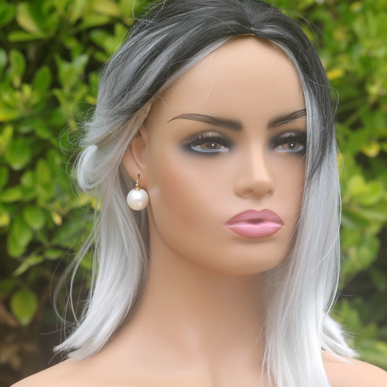 May include: A pair of white pearl drop earrings with gold hooks. The earrings are worn by a mannequin with silver and black hair.