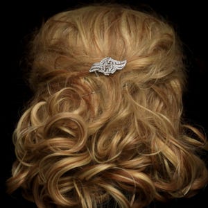 May include: A silver hair comb with a crystal design. The comb is in a woman's hair.