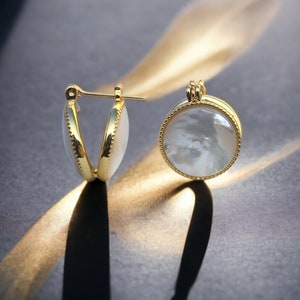 May include: A pair of gold hoop earrings with a white mother-of-pearl inlay. The earrings are round and have a delicate gold trim.