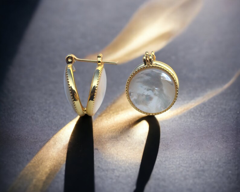May include: A pair of gold hoop earrings with a white mother-of-pearl inlay. The earrings are round and have a delicate gold trim.