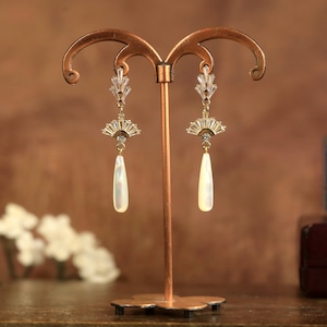 Op de afbeelding: Een paar gouden oorbellen met een waaiervormig ontwerp en een traanvormige parel hanger.