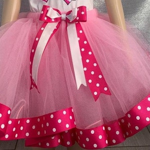 Può includere: Gonna tutu in tulle rosa con un bordo di nastro a pois bianchi e rosa. La gonna ha un fiocco di raso bianco con pois rosa.