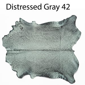 K&ouml;nnte beinhalten: Ein St&uuml;ck Leder mit einem abgenutzten grauen Finish und einer strukturierten Oberfl&auml;che. Der Text Distressed Gray 42 ist &uuml;ber dem Fell abgedruckt. Das Material hat eine unregelm&auml;&szlig;ige, organische Form mit nat&uuml;rlichen Kanten und einem fleckigen Aussehen.