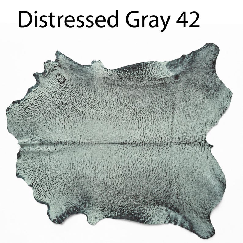 K&ouml;nnte beinhalten: Ein St&uuml;ck Leder mit einem abgenutzten grauen Finish und einer strukturierten Oberfl&auml;che. Der Text Distressed Gray 42 ist &uuml;ber dem Fell abgedruckt. Das Material hat eine unregelm&auml;&szlig;ige, organische Form mit nat&uuml;rlichen Kanten und einem fleckigen Aussehen.