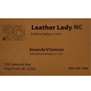 May include: A business card with a textured, tan background. The card features the text "Leather Lady NC" and contact information, including a website, email, and phone number. The card also includes the address 709 Lakecrest Ave., High Point, NC 27265.