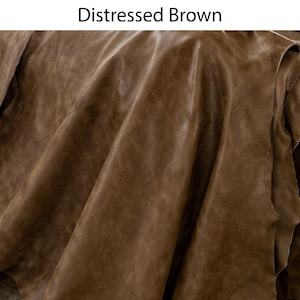 K&ouml;nnte beinhalten: Ein St&uuml;ck Leder mit einem abgenutzten braunen Finish, das eine nat&uuml;rliche Narbenstruktur und sichtbare Falten aufweist. Der Text Distressed Brown ist oben im Bild aufgedruckt und gibt die Farbe und Art des gezeigten Materials an.
