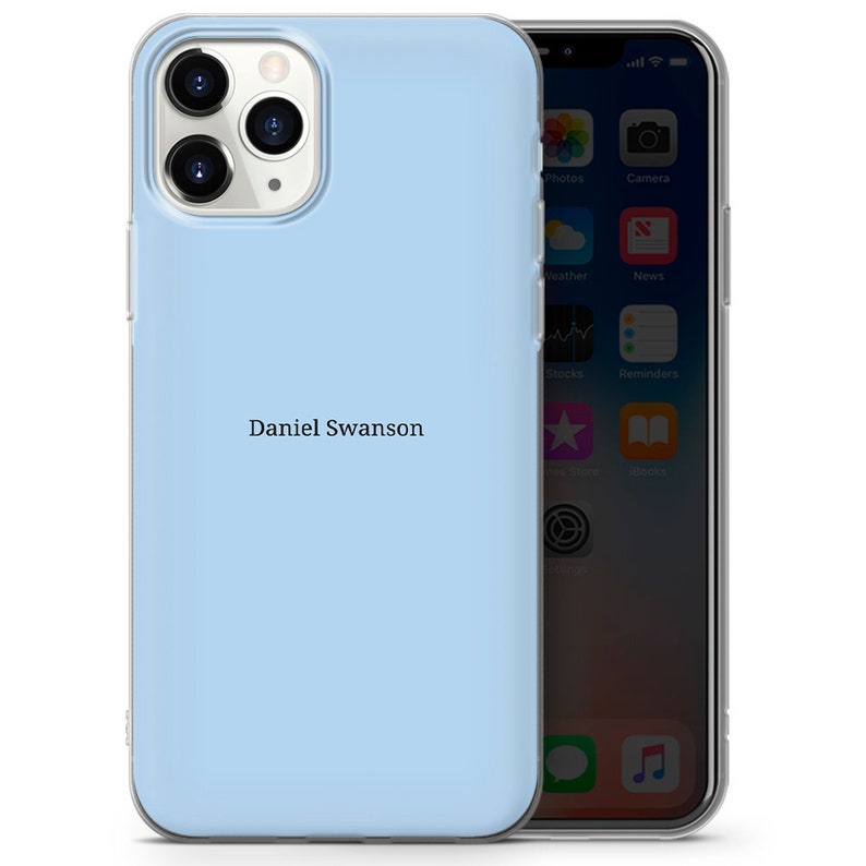 May include: A light blue phone case with a clear back. The case has a personalized name, "Daniel Swanson", printed on the back.