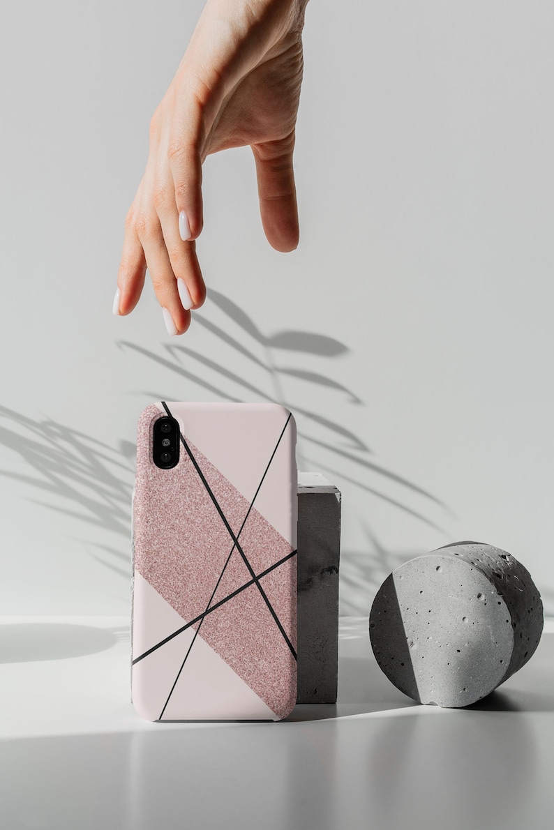 May include: A pink and black geometric phone case with glitter accents. The case is sitting on a gray concrete block and a gray concrete cylinder.