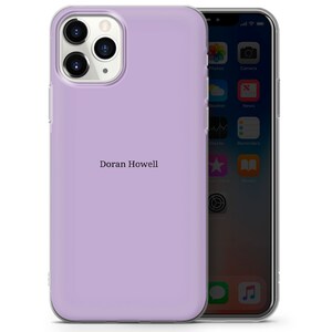 May include: A lavender phone case with a clear back and a clear front. The case has a raised camera bump and a clear border around the edges. The case has the name "Doran Howell" printed on the back.