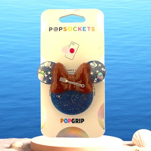 May include: A blue and brown PopSocket phone grip with a fork and bow design. The grip is on a white card with the words "PopSockets" and "PopGrip" printed on it.