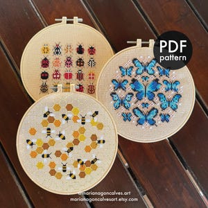 Peut inclure: Trois motifs de point de croix dans des cerceaux en bois. L'un pr&eacute;sente des col&eacute;opt&egrave;res color&eacute;s, un autre des papillons bleus et le troisi&egrave;me des abeilles et des nids d'abeilles. Le cercle noir en haut &agrave; droite indique "PDF pattern". Le texte "@marianagoncalves.art marianagoncalvesart.etsy.com" est en bas.