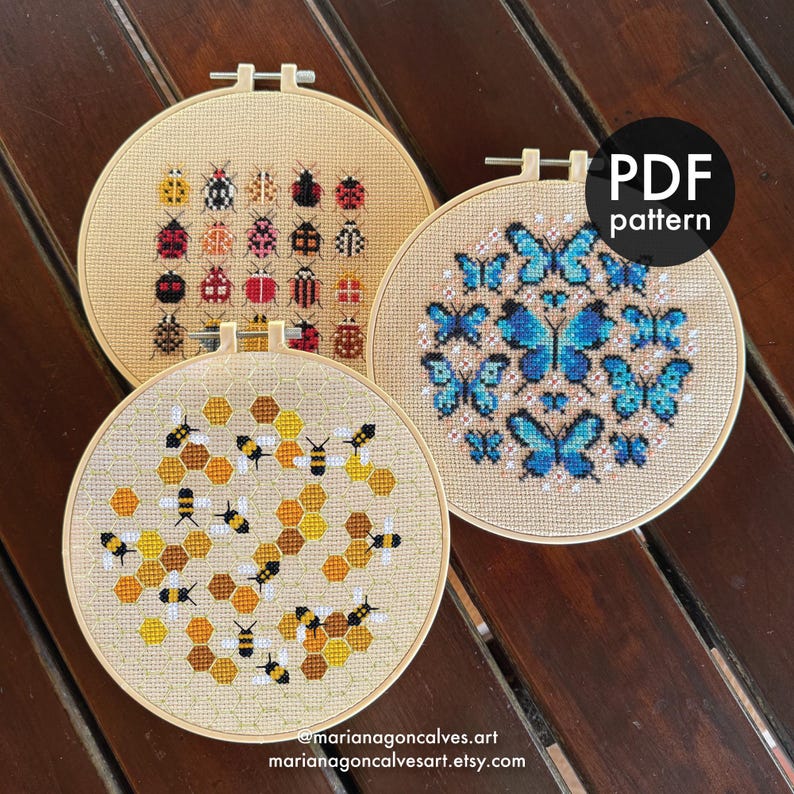 Peut inclure: Trois motifs de point de croix dans des cerceaux en bois. L'un pr&eacute;sente des col&eacute;opt&egrave;res color&eacute;s, un autre des papillons bleus et le troisi&egrave;me des abeilles et des nids d'abeilles. Le cercle noir en haut &agrave; droite indique "PDF pattern". Le texte "@marianagoncalves.art marianagoncalvesart.etsy.com" est en bas.