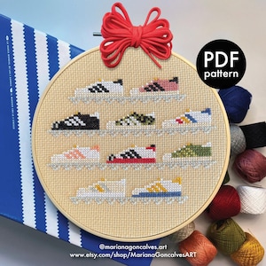 May include: A cross-stitch embroidery hoop displaying various colourful trainers. The trainers are arranged in rows on a beige fabric, with a red bow at the top. The text "PDF pattern" is in a black circle. The artist's Etsy shop URL is at the bottom.