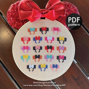 May include: A cross-stitch pattern in a round hoop featuring colorful Mickey Mouse ear designs. The hoop is set against a wooden surface, with a red sequined bow and ears in the background. The text "PDF pattern" is visible.