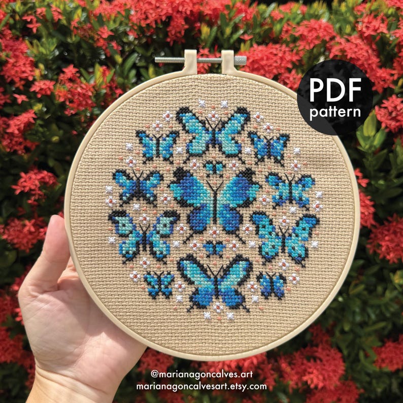 Peut inclure: Un cercle de broderie au point de croix avec un motif circulaire de papillons bleus. Les papillons sont dispos&eacute;s sym&eacute;triquement sur un tissu beige. Le texte "PDF pattern" est visible. L'URL de la boutique Etsy est &eacute;galement visible.
