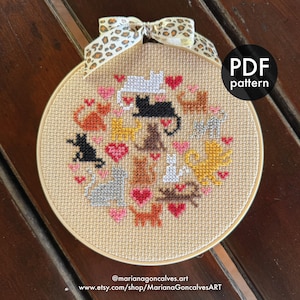 May include: A cross-stitch embroidery hoop featuring a pattern of various cat breeds and pink hearts on a beige background. The hoop is adorned with a leopard print ribbon. The text "PDF pattern" is visible. The artist's name and Etsy shop URL are also displayed.