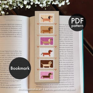 May include: A cross-stitch pattern bookmark featuring six rectangular frames, each containing a pixelated dog in various shades of brown, tan, and pink. The design is printed on a beige grid background with small orange accents between the frames.
