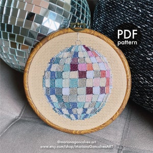 May include: A cross-stitch pattern of a disco ball in a wooden embroidery hoop. The disco ball is made of squares in shades of blue, pink, purple, and orange. The text "PDF pattern" is visible. The artist's Etsy shop URL is also visible.