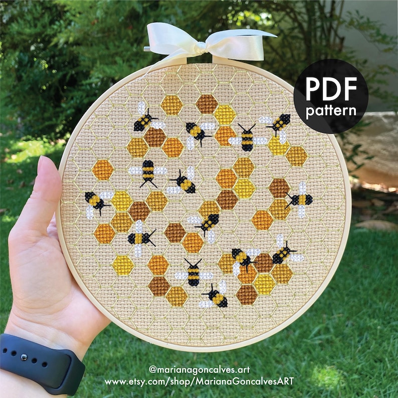 Peut inclure: Un cercle de broderie au point de croix avec un motif de nid d'abeilles et d'abeilles. Le design utilise des nuances de jaune, de marron et de noir. Le texte "PDF pattern" est visible. Le cercle est orn&eacute; d'un ruban blanc.