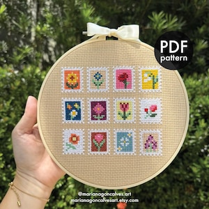 Puede incluir: Un bastidor de bordado de punto de cruz con un diseño floral. El diseño incluye doce pequeñas imágenes cuadradas de varias flores en diferentes colores. El texto "PDF pattern" es visible. También se muestra el nombre y el sitio web del artista.