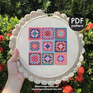 Puede incluir: Un patrón de punto de cruz en un aro beige con un borde de ganchillo. El diseño presenta nueve cuadrados coloridos con patrones florales y geométricos en tonos de rosa, azul y naranja. El texto en la imagen dice "PDF pattern" y el sitio web del artista.