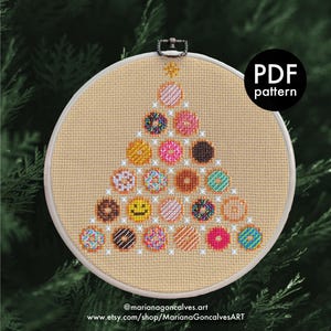 Könnte beinhalten: Ein Kreuzstichmuster eines Weihnachtsbaums aus Donuts in einem Stickrahmen. Die Donuts sind in verschiedenen Farben und Designs gehalten, darunter Streusel und Zuckerguss. Der Text "PDF pattern" befindet sich in einem schwarzen Kreis. Die Website des Künstlers ist unten.