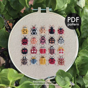 Peut inclure: Un motif de point de croix repr&eacute;sentant une collection de col&eacute;opt&egrave;res color&eacute;s et stylis&eacute;s. Le motif est pr&eacute;sent&eacute; dans un cercle &agrave; broder avec un fond en tissu beige. Le texte "PDF pattern" est visible, ainsi que les coordonn&eacute;es de l'artiste.
