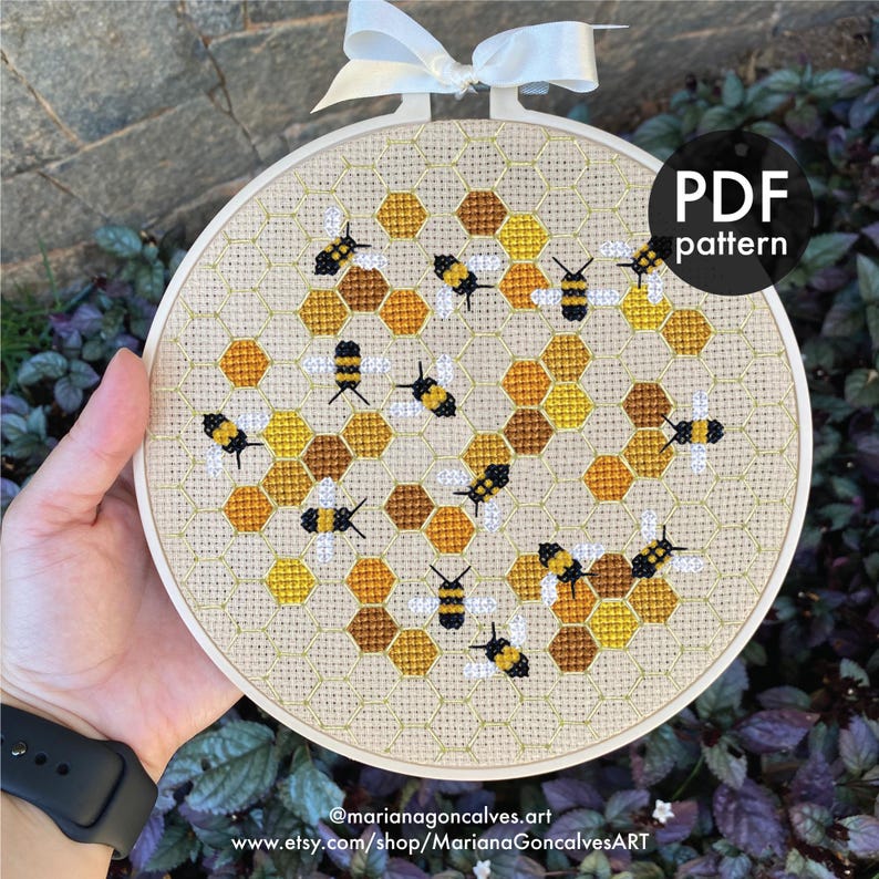 Peut inclure: Broderie au point de croix dans un cercle, repr&eacute;sentant un motif en nid d'abeilles avec des abeilles. Le design utilise des nuances de jaune, marron et noir. Un ruban blanc est attach&eacute; en haut. Le texte "PDF pattern" est visible.