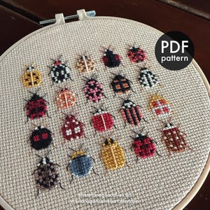Peut inclure: Un tambour de broderie au point de croix avec divers motifs d'insectes color&eacute;s. Les insectes sont brod&eacute;s dans diff&eacute;rentes couleurs et motifs, dont le rouge, le noir, le jaune et le blanc. Le texte "PDF pattern" est visible.