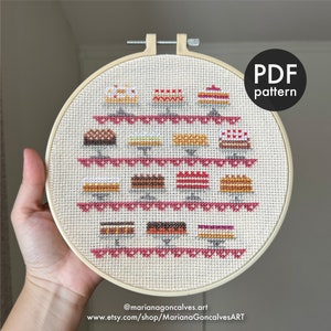 Puede incluir: Un patrón de punto de cruz de un soporte para pasteles con 18 pasteles diferentes, incluyendo chocolate, fresa y limón. El patrón está en un aro y el texto "PDF pattern" está en la esquina superior derecha.