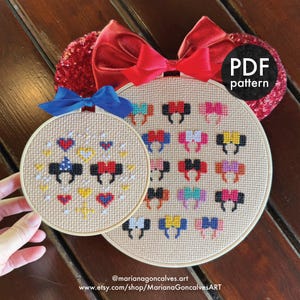 Pode incluir: Dois padrões de ponto cruz em bastidores de bordado. Um apresenta desenhos coloridos de orelhas do Mickey Mouse, o outro tem orelhas do Mickey e corações. Uma fita vermelha com lantejoulas e uma fita azul estão presas. O texto diz "PDF pattern".
