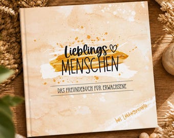 May include: A hardcover book with a beige watercolor-style cover. The cover features the German text "Lieblings Menschen" in black script and a gold brushstroke design. The text "DAS FREUNDEBUCH FUR ERWACHSENE" is also visible.