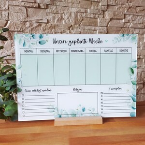 Könnte beinhalten: Ein weißer Trockenlösch-Wochenplaner mit grünem Blumendesign. Der Planer hat Abschnitte für jeden Tag der Woche, eine To-Do-Liste, Notizen und einen Essensplan.