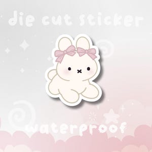 May include: A die-cut sticker featuring a cream-colored bunny with pink bows on its ears. The bunny has a black cross for a mouth and black dot eyes. The word "waterproof" is written below the bunny.