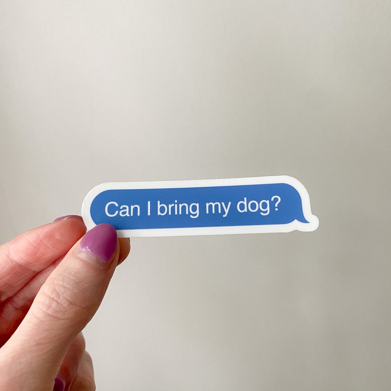 Hand holding “Can I bring my dog?” sticker in front of soft neutral backdrop.