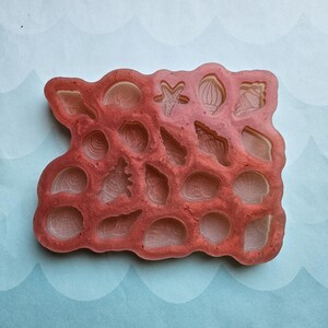 May include: A red silicone mold with 18 different shapes of seashells, starfish, and other ocean-themed designs.