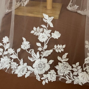 K&ouml;nnte beinhalten: Wei&szlig;er Braut Schleier mit zarter floraler Spitzen Stickerei. Die Spitze zeigt ein sich wiederholendes Muster aus kleinen Blumen und Bl&auml;ttern.