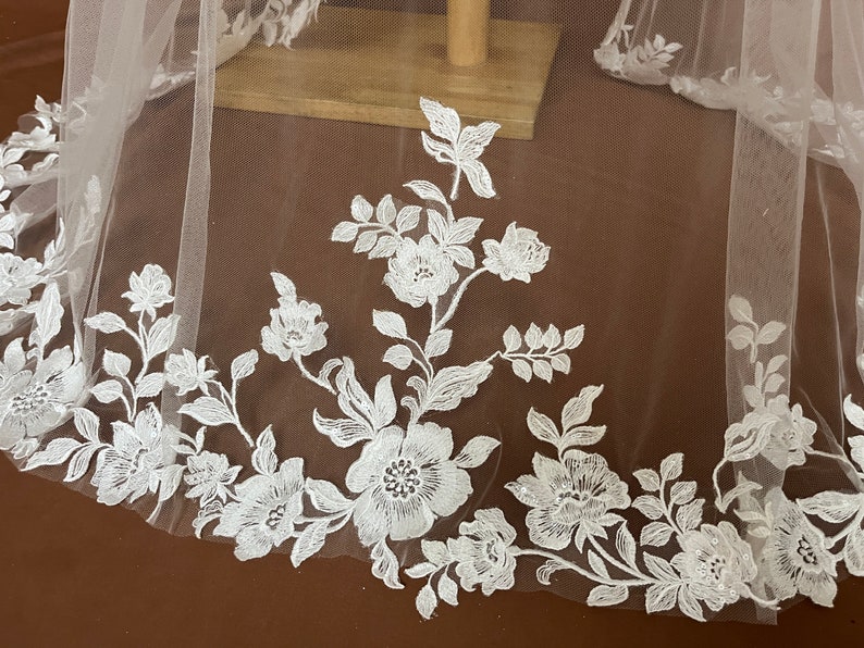 K&ouml;nnte beinhalten: Wei&szlig;er Braut Schleier mit zarter floraler Spitzen Stickerei. Die Spitze zeigt ein sich wiederholendes Muster aus kleinen Blumen und Bl&auml;ttern.