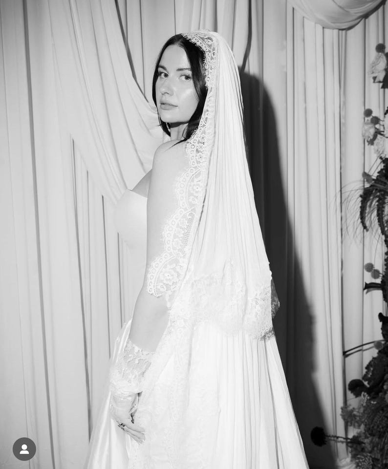Puede incluir: Fotograf&iacute;a en blanco y negro de una novia con un vestido de novia blanco y un velo. El velo presenta delicados detalles de encaje, y el vestido tiene un dise&ntilde;o simple y elegante. La novia mira por encima del hombro.