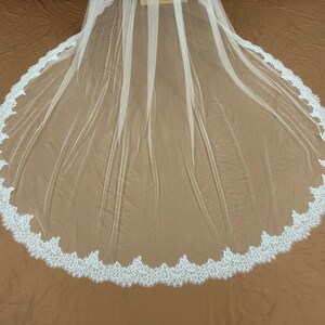 Puede incluir: Un velo de novia blanco con un ribete de encaje festoneado. El velo est&aacute; hecho de una tela transparente y ligera y est&aacute; dise&ntilde;ado para ser usado sobre la cabeza y los hombros. El ribete de encaje a&ntilde;ade un toque delicado y elegante.