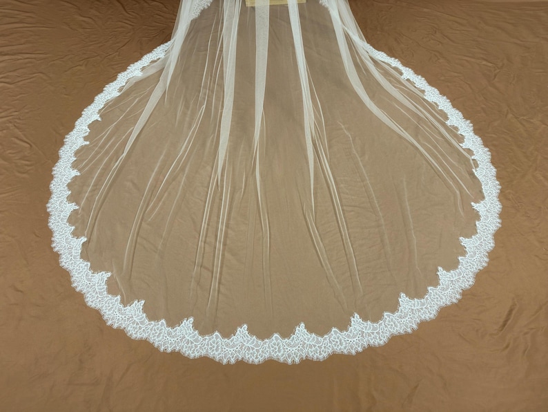Puede incluir: Un velo de novia blanco con un ribete de encaje festoneado. El velo est&aacute; hecho de una tela transparente y ligera y est&aacute; dise&ntilde;ado para ser usado sobre la cabeza y los hombros. El ribete de encaje a&ntilde;ade un toque delicado y elegante.