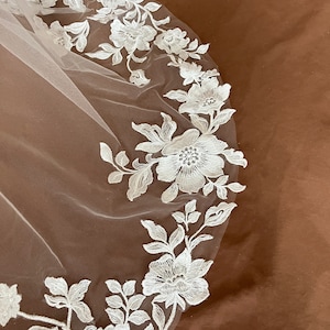 K&ouml;nnte beinhalten: Wei&szlig;er Braut Schleier mit zarter floraler Spitzen Stickerei. Die Spitze zeigt ein sich wiederholendes Muster aus Blumen und Bl&auml;ttern.