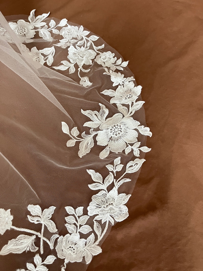 K&ouml;nnte beinhalten: Wei&szlig;er Braut Schleier mit zarter floraler Spitzen Stickerei. Die Spitze zeigt ein sich wiederholendes Muster aus Blumen und Bl&auml;ttern.