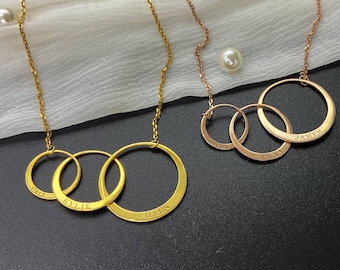 May include: Gold and rose gold necklaces with interlocking circles engraved with names. The gold necklace has the names "Cali", "Kylie", and "Allen". The rose gold necklace has the names "Taylor", "Luna", and "James".