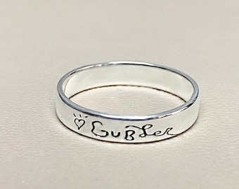May include: A silver band ring with the inscription "♡ SUB Lee" engraved on the outside.