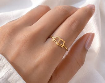 May include: A gold-toned ring featuring a delicate, open-work design shaped like an open book. The band is thin and circular, with the book motif centered on the top. The metal has a smooth, polished finish that reflects light across its surface.