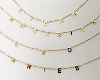 May include: Four gold necklaces with zodiac signs spelled out in individual letters. The necklaces are layered on top of each other. The signs are Libra, Aquarius, Leo, and Aries.
