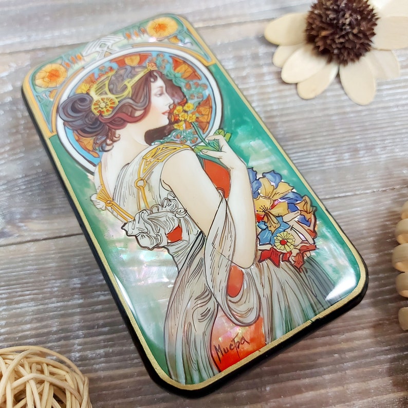May include: A rectangular wooden box with a green, iridescent, and gold painted design. The box features a woman in a white dress holding a bouquet of flowers. The box is signed "Mucha" in the bottom right corner.
