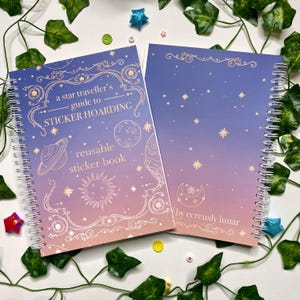 May include: A reusable sticker book with a celestial theme. The cover features a pink and purple gradient with gold foil accents. The title is "a star traveller's guide to STICKER HOARDING" and the subtitle is "reusable sticker book". The book is by cereusly lunar.