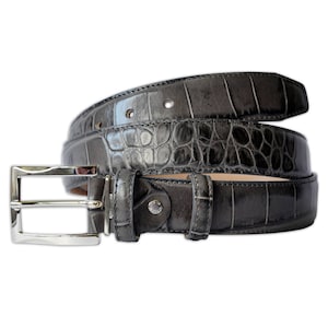 May include: A dark grey belt featuring a glossy, embossed crocodile skin texture. The belt includes a polished silver-tone rectangular metal buckle, a matching leather keeper loop, and a series of circular adjustment holes along the strap.